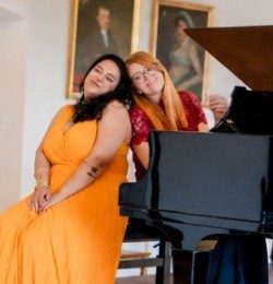 Zwei Frauen am Klavier in einem Saal mit Gemälden